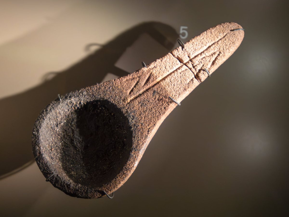 An engraved stone object with a hollowed bowl, shown against a dark background