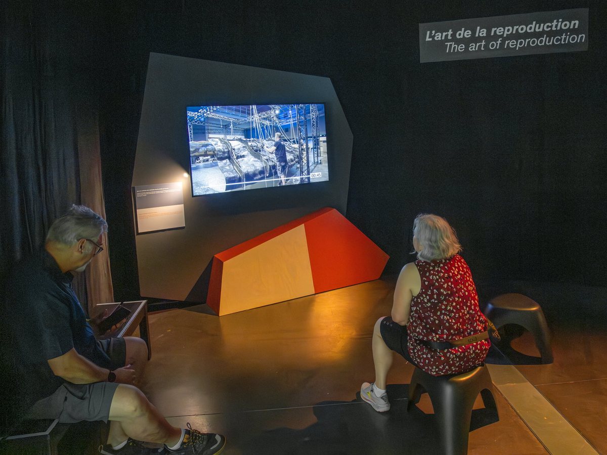 Two visitors seated in front of the “The art of reproduction” module, where a film shows a facsimile under construction