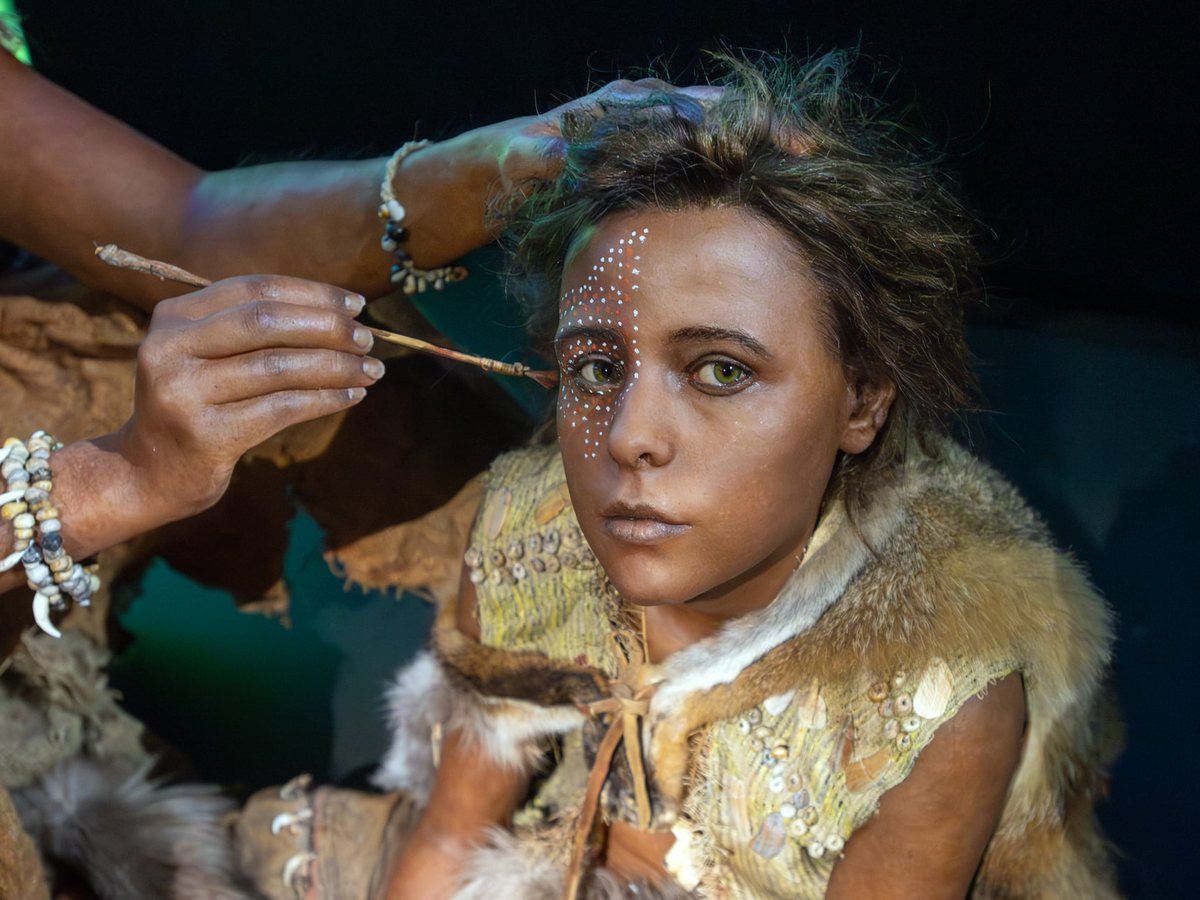 A hand applying white pigment to the face of a reconstructed adolescent